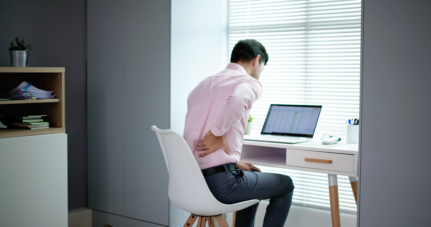 Back Pain from Desk Job? Here’s How to Fix It, A person sitting at their desk with their hand on their lower back in pain