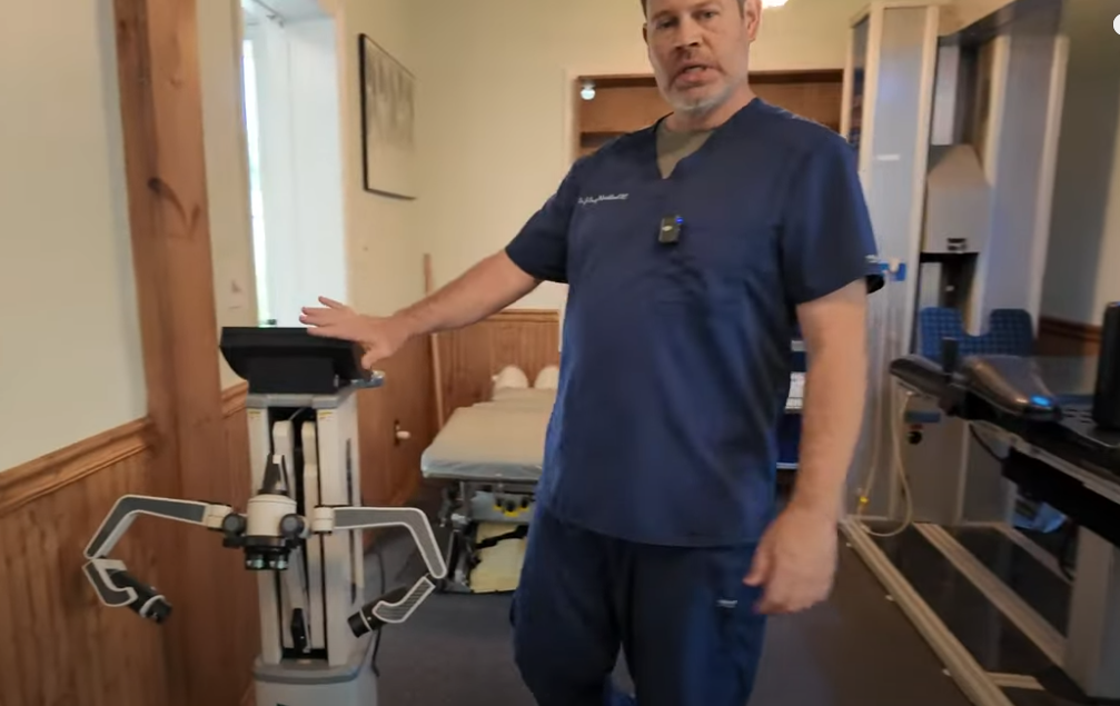 A person standing in a room pointing to specialized chiropractic equipment