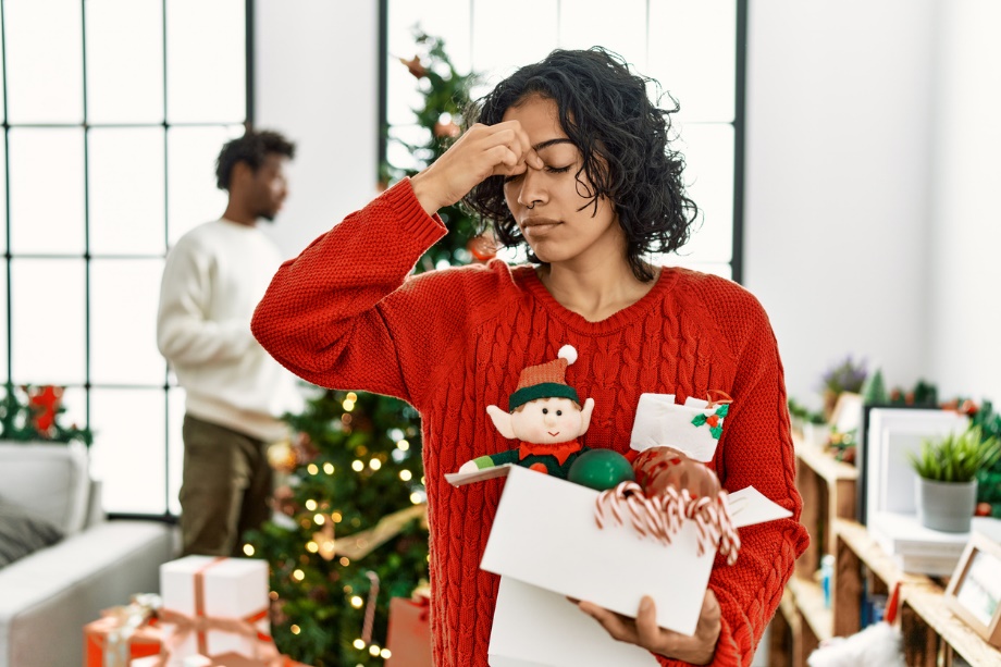 A person holding a box of presents and pinching the bridge of their nose