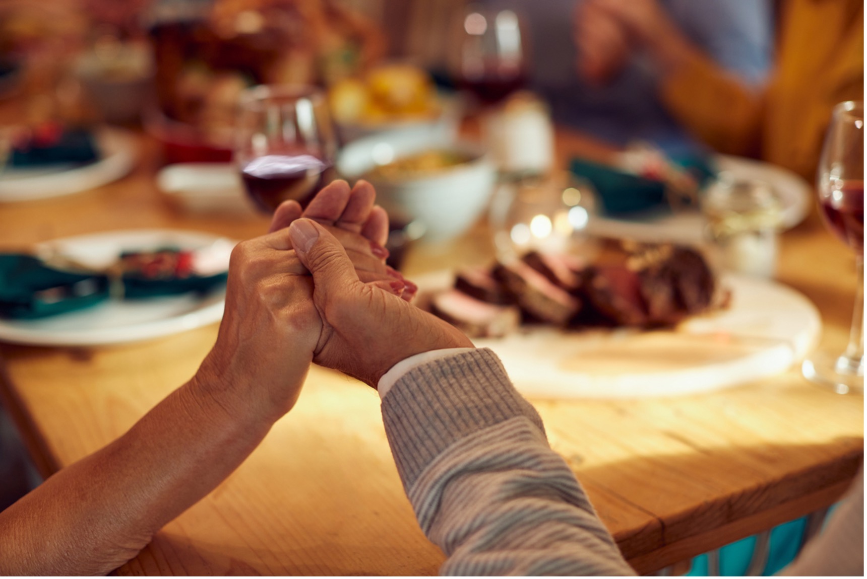 People joined in hand sitting around a thanksgiving dinner table