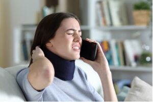 A person holding their neck, in. A neck brace, talking a phone