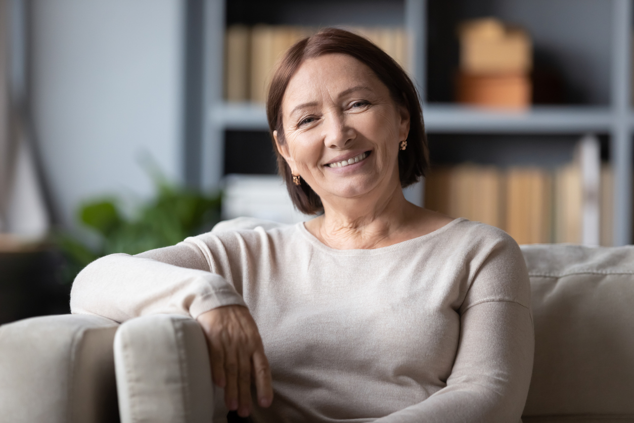 Smiling older woman with short brown hair sitting on a couch.