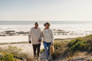 Thankful for Relief: How Chiropractic Care Restores Comfort and Mobility in Little River, SC, Cheerful elderly couple smiling happily while walking away from the beach after a picnic. Romantic senior couple enjoying a seaside getaway after retirement.