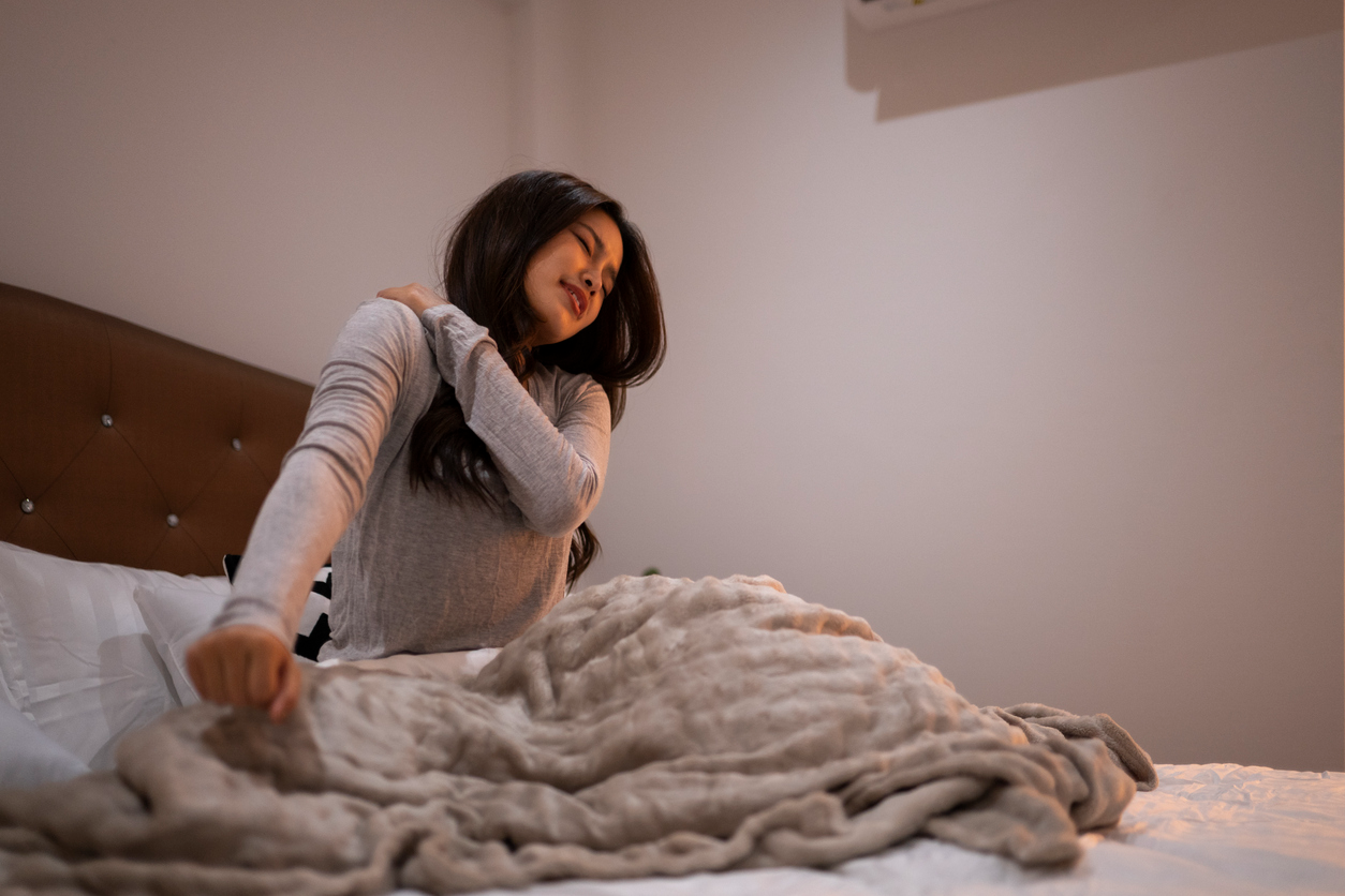 A woman in bed holding her shoulder with nighttime pain after waking.