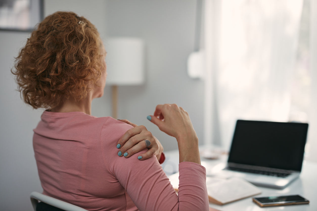 A woman holding her painful shoulder while working at a desk.