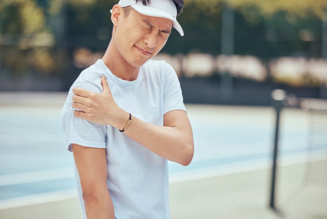 Man holding his shoulder in discomfort while playing tennis, showing strain from repetitive activity